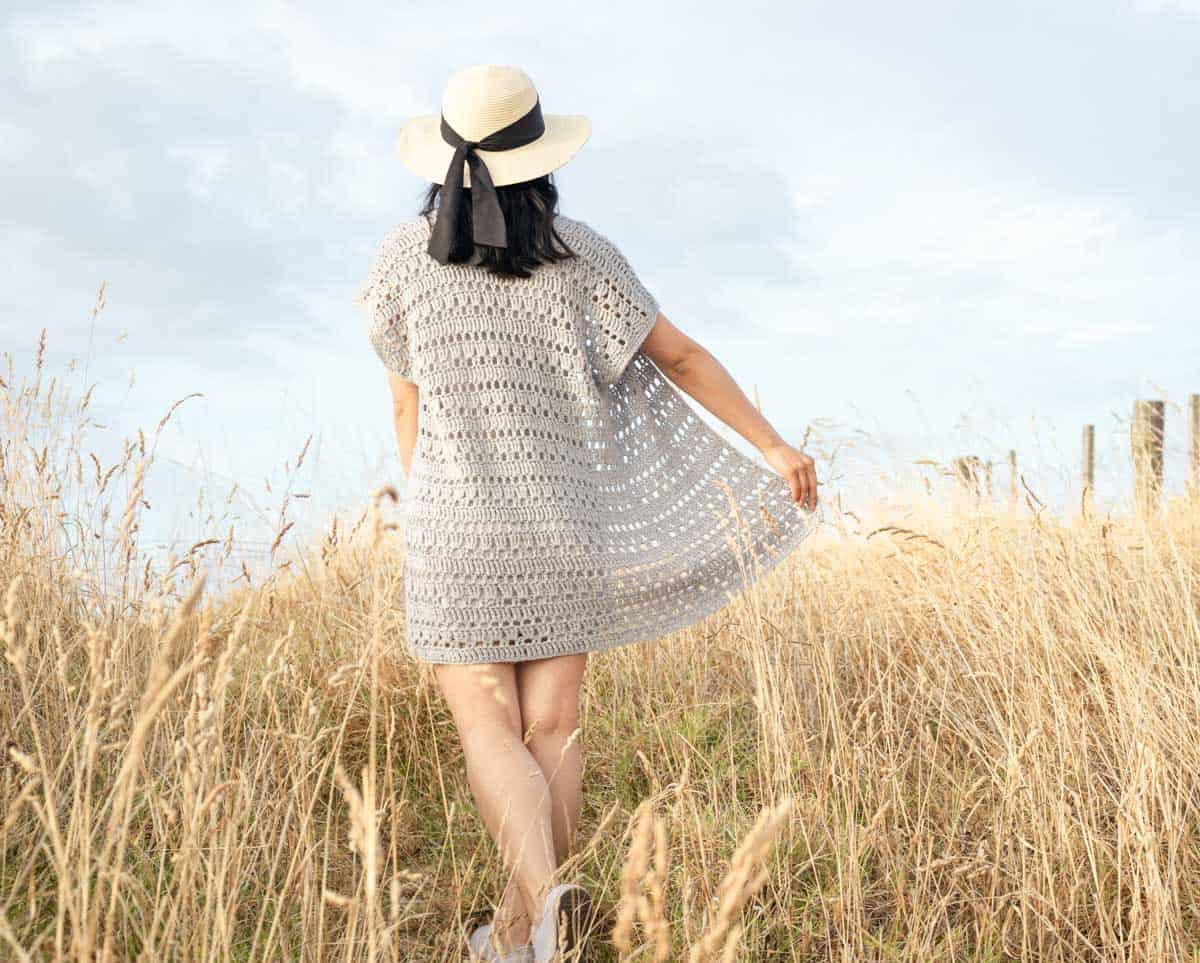 back view of a woman wearing the Summer Crochet Cardigan and a hat in field